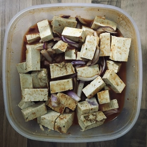 Kunststoffdose mit groben Tofustücken, Zwiebeln und Marinade