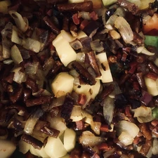 Topf gefüllt mit angebratenen Kabanossi und Zwiebel, Kartoffel und weiteren Gemüse, bevor diese mit der Gemüsebrühe aufgegossen werden.