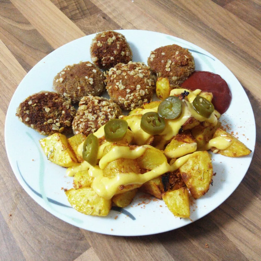 Gebratene Nuggets mit Kartoffelecken, Käsesoße, Jalapenos und Ketchup auf einem Teller